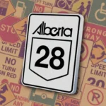 Белый прямоугольный знак с логотипом "Alberta" и номером "28" внутри контура щита. Знак "Provincial Highway Route Marker" указывает номер провинциального шоссе