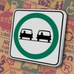 Белый квадрат с зеленым кольцом, внутри которого изображены два автомобиля. Предписывающий знак "Passing Permitted", разрешающий обгон