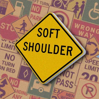 Желтый ромб с черной надписью "SOFT SHOULDER". Знак "Soft Shoulder" предупреждает о мягкой или рыхлой обочине, на которую опасно съезжать
