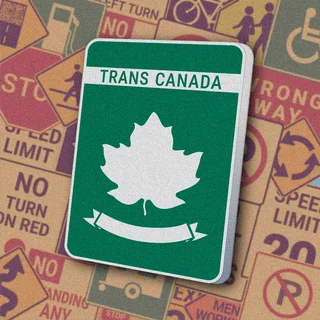 Зеленый прямоугольный знак с белой надписью "TRANS CANADA" вверху и белым кленовым листом на зеленом фоне с декоративной лентой. Знак "Trans-Canada Highway" обозначает маршрут Трансканадского шоссе — главной национальной автомагистрали Канады